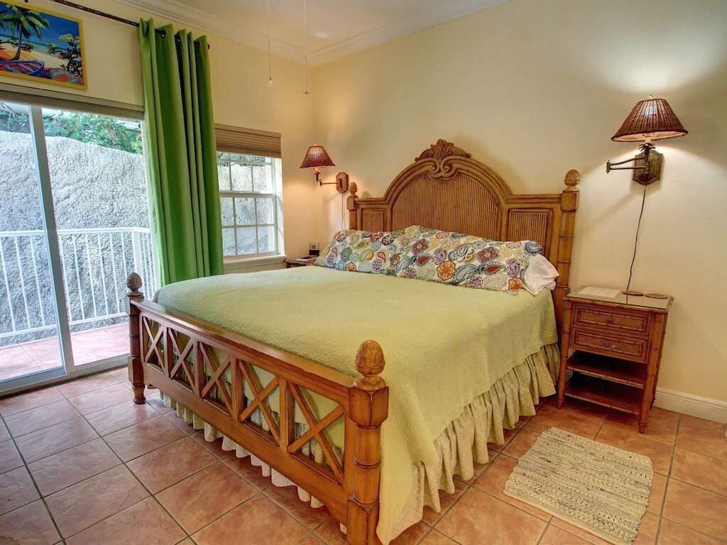 A bedroom with a wooden bed, a green curtain, a window with a view, a nightstand, and a lamp.
