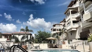 A hotel pool area with lounge chairs and umbrellas, surrounded by multi-story buildings with balconies.
