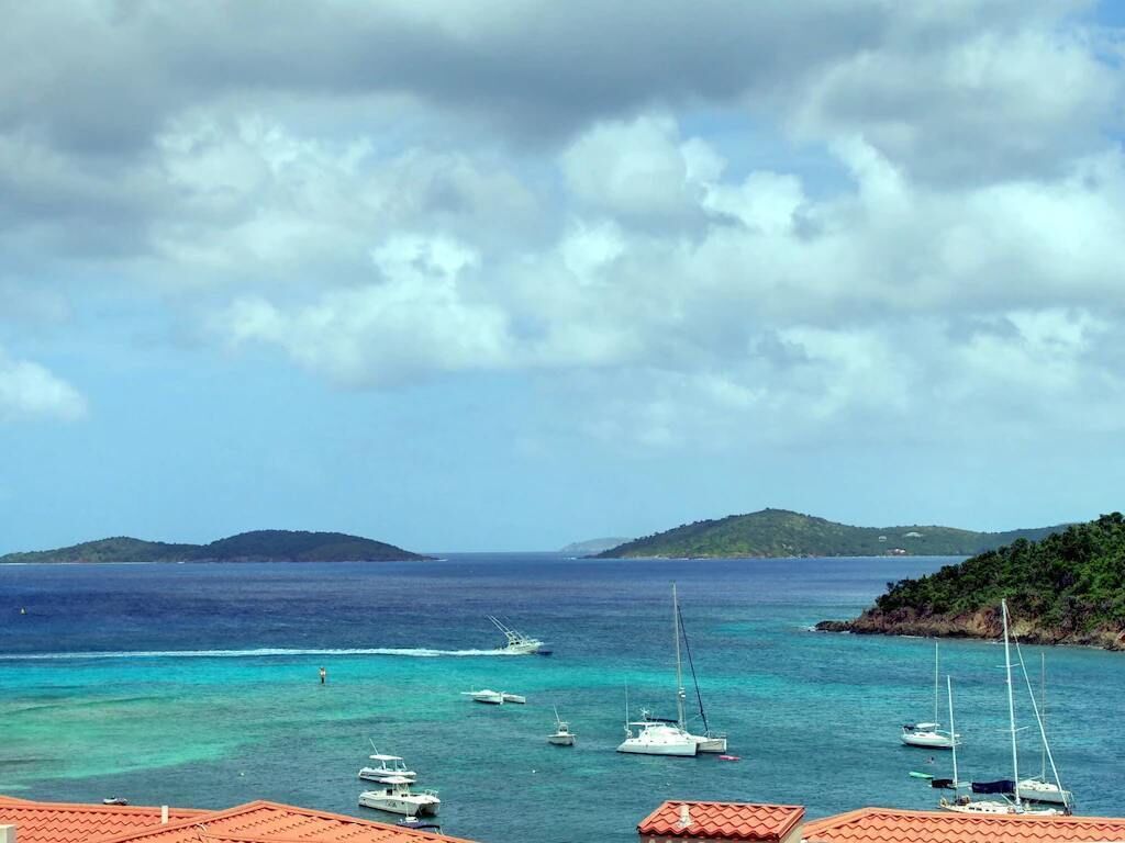A coastal view with boats anchored near a building with red-tiled roofs.