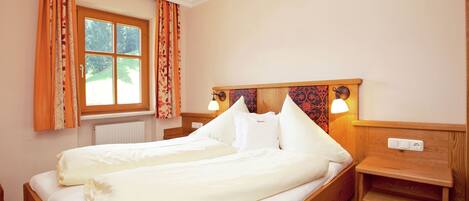 A neatly made bed in a room with a wooden headboard, two bedside lamps, and a window with curtains.
