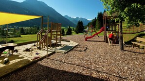 A playground with a slide and climbing structures, surrounded by a gravel area and a yellow canopy. - Apartment in Kleinarl Near Ski Slopes (Kleinarl)
