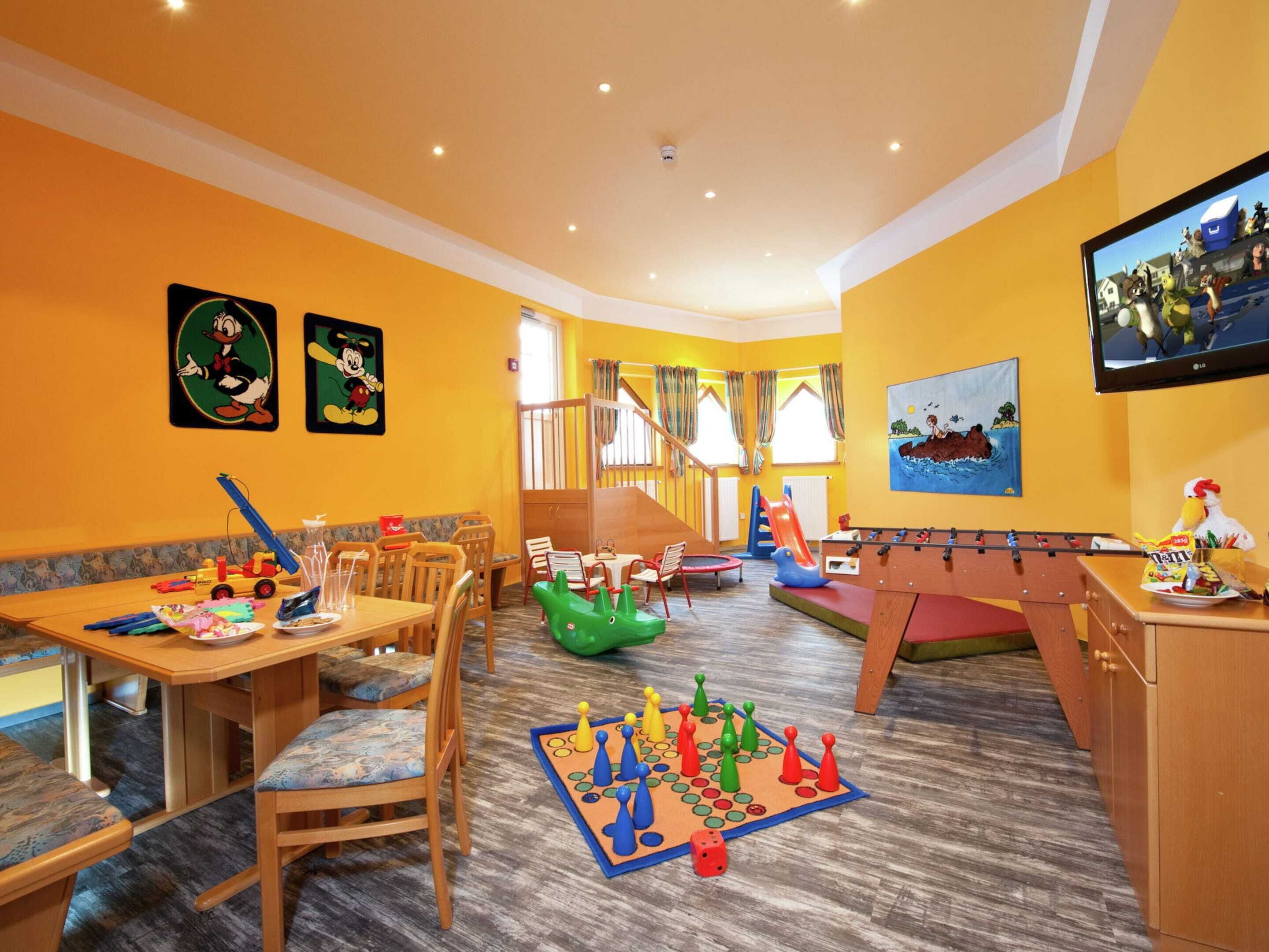 A children's play area with a foosball table, a slide, and a table with toys and snacks.