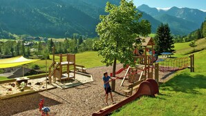 A playground with a slide and climbing structures, surrounded by a grassy area and a view of mountains. - Apartment in Kleinarl Near Ski Slopes (Kleinarl)