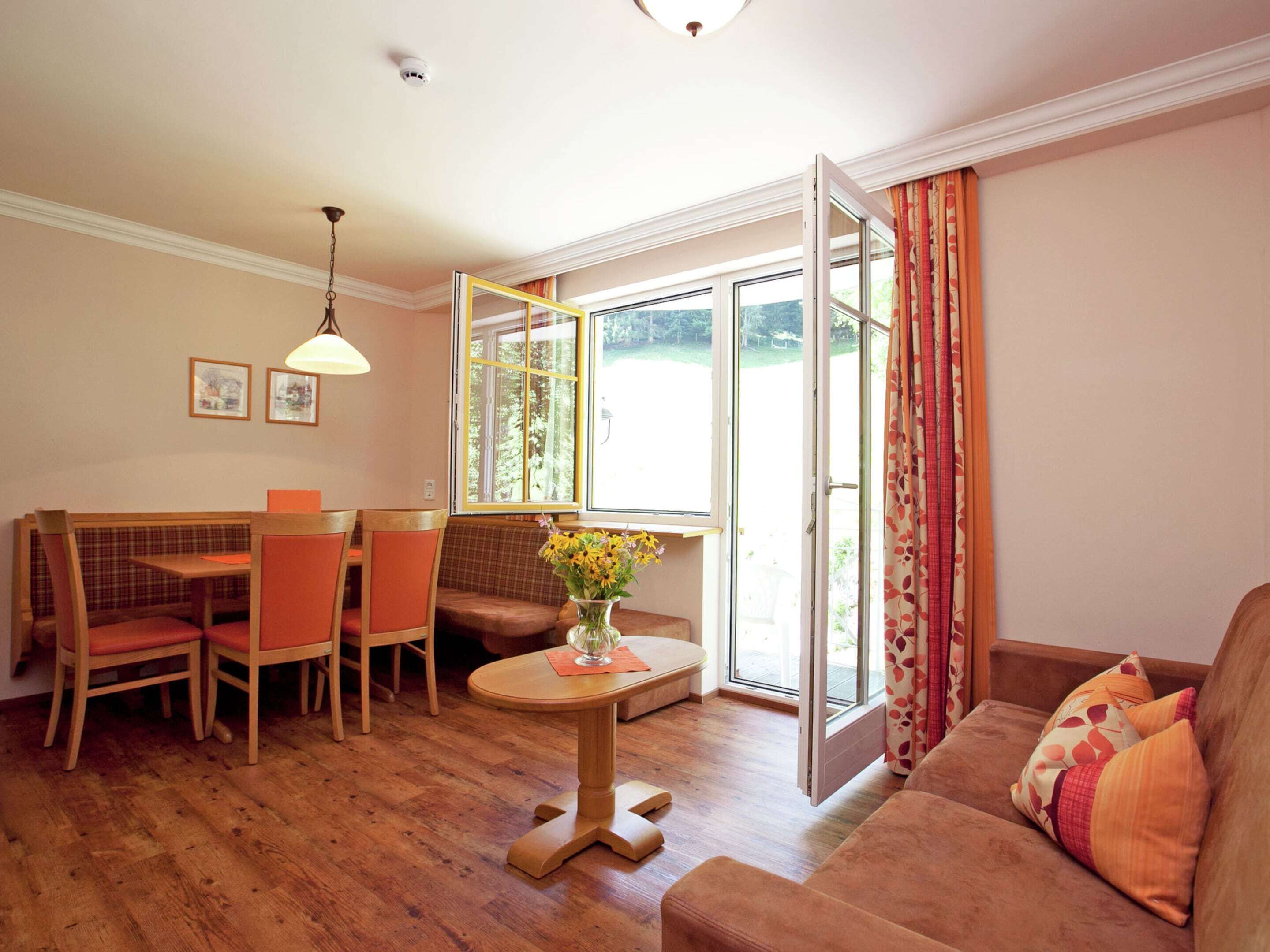 Un salon chaleureux avec un plancher en bois, un canapé, une table à manger avec des chaises et une fenêtre avec des rideaux.