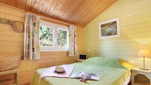 Una stanza in legno con un letto, una finestra con tende, un laptop su un comodino e una lampada.