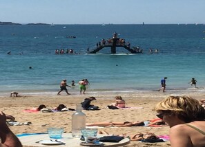 A beach with people sunbathing and swimming, a pier with people on it, and boats in the water. - Apartment in France With Modern Design (Roz-sur-Couesnon)