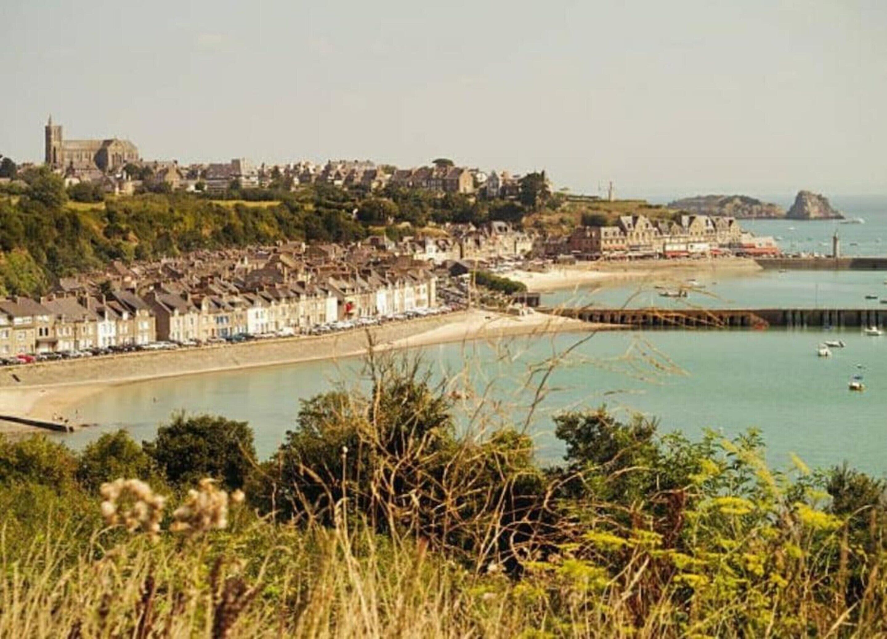 A coastal town with a prominent church, a sandy beach, and a rocky outcrop in the distance.