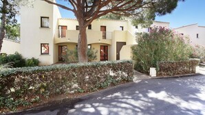 A multi-story building with balconies, a tree in the foreground, and a hedge along the sidewalk. - Apartment in Saint-loup Amid Pine Trees (Agde)