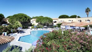 A pool with lounge chairs and umbrellas, surrounded by greenery and buildings. - Apartment in Saint-loup Amid Pine Trees (Agde)