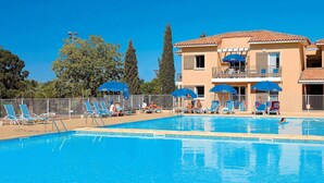 A swimming pool with lounge chairs and umbrellas, a building with balconies, and trees in the background. - Sunny Retreat With Pool (La Londe-les-Maures)