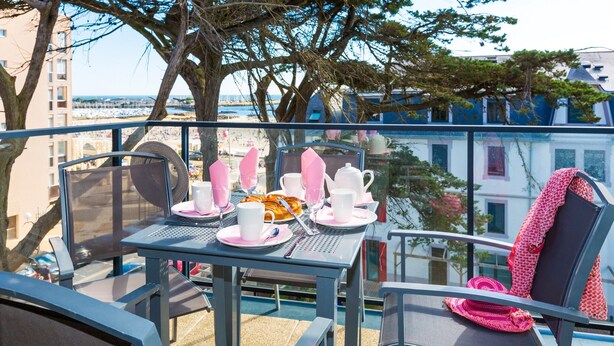 Ein Balkon mit Frühstückstisch, mit Blick auf Strand und Gebäude.