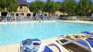En swimmingpool med solstolar och parasoller, omgiven av träd och en byggnad.