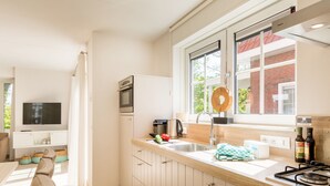 A modern kitchen with a built-in oven, a sink, and a stove. There is a window with a view of a brick building and greenery outside. - Villa in Dishoek Near Noordzee Beach (Koudekerke)