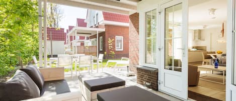 A covered patio area with outdoor seating, a brick wall, and a view into the house.