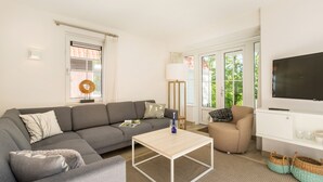 A modern living room with a grey sofa, a wooden coffee table, a beige armchair, a floor lamp, and a TV on a white cabinet. - Villa in Dishoek Near Noordzee Beach (Koudekerke)