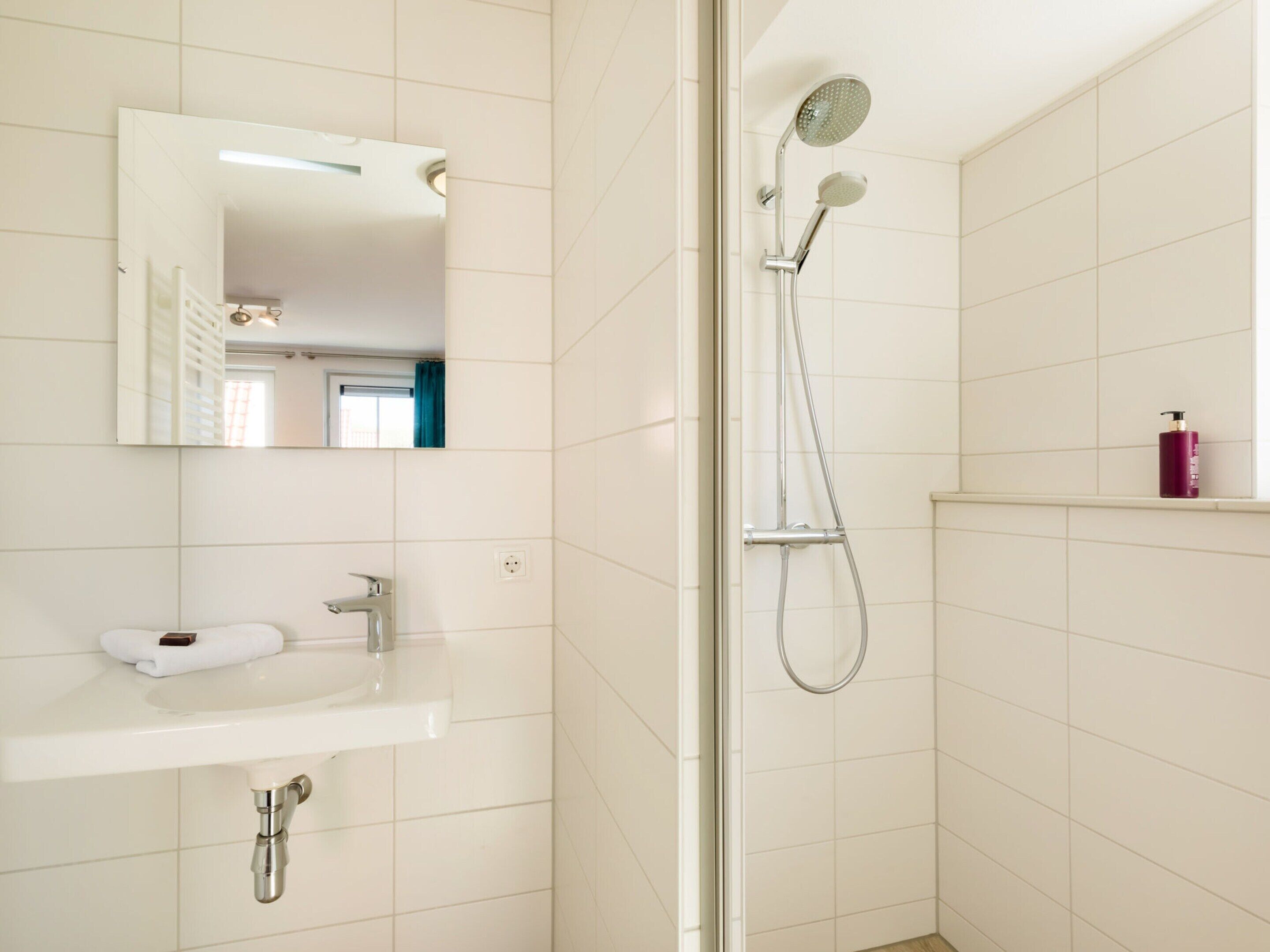 A modern bathroom with a white sink, mirror, and shower.