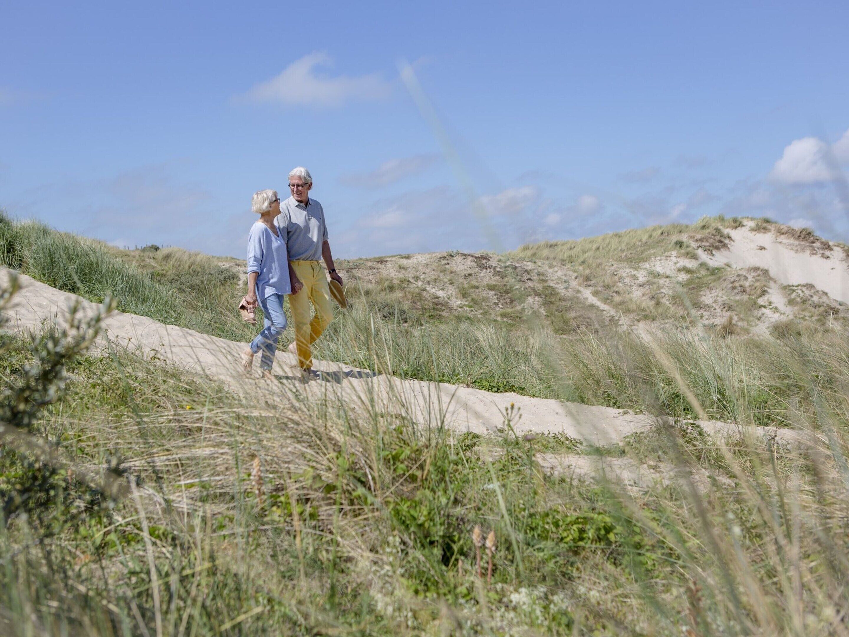 Uma trilha de areia com grama e dunas ao fundo.