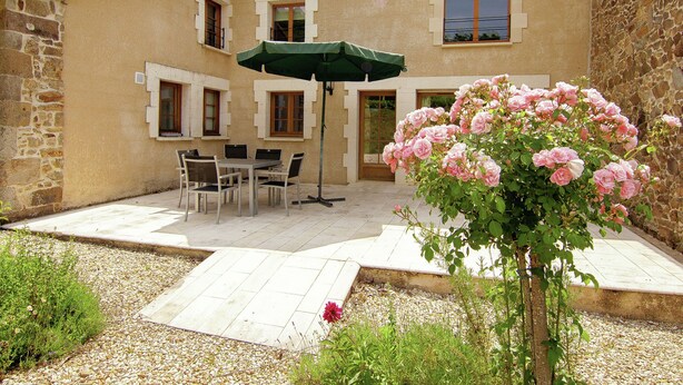 Un patio con una mesa, sillas, un parasol verde y un rosal.
