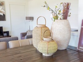 Uma mesa de jantar com duas lanternas de fibra e um vaso grande com flores.