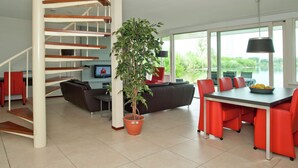 A modern interior with a spiral staircase, a dining area with red chairs, a large potted plant, and a view of greenery outside. - Villa on a Beautiful Resort With Sauna and View (Heel)