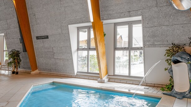 Une piscine intérieure offrant une vue dégagée sur l’eau, avec un plafond en bois et un panneau indiquant la présence d’une aire de jeux aquatique.