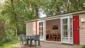Une petite cabane dotée d’une terrasse, d’une table avec des chaises et d’une porte rouge.