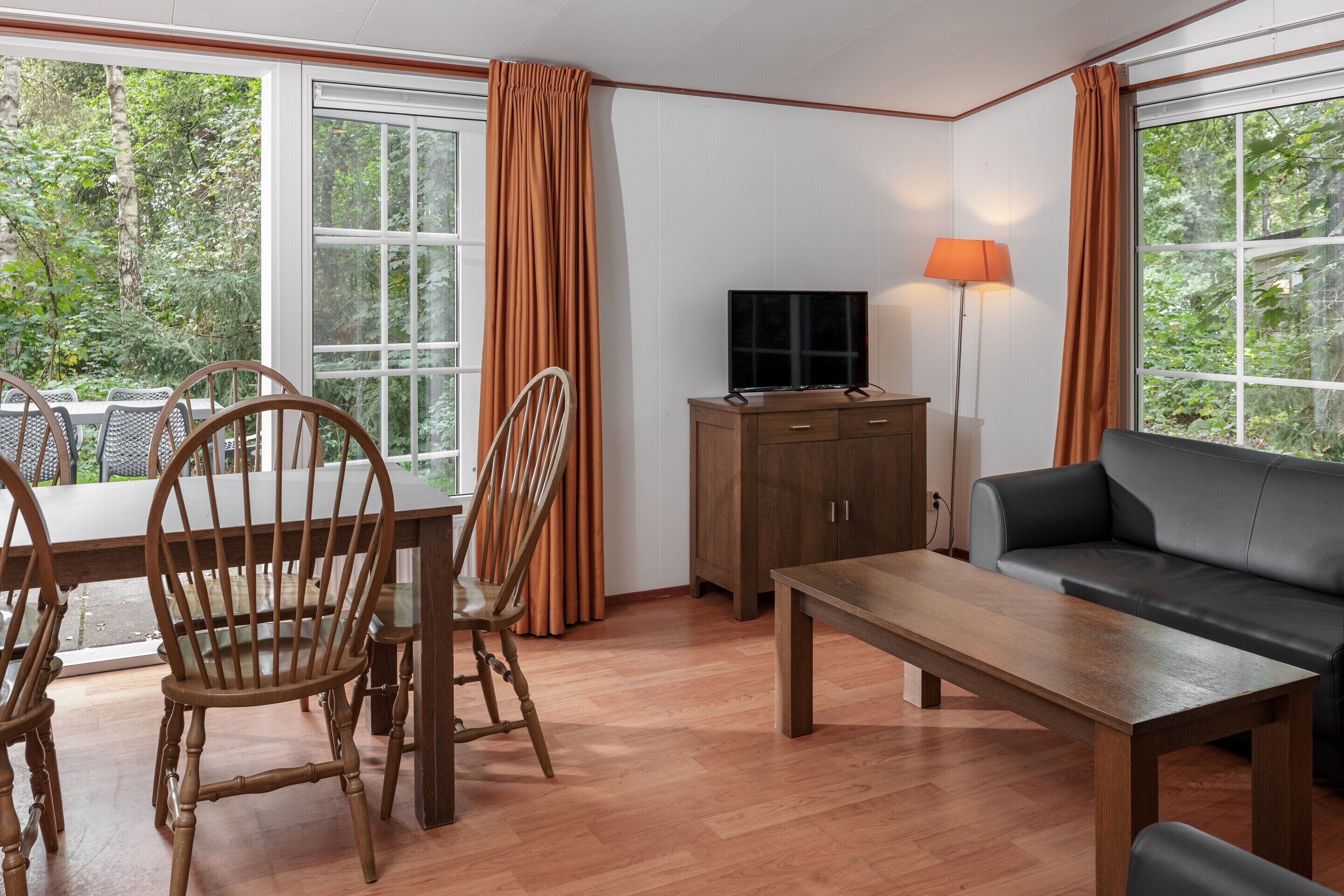 A room with a wooden dining table, chairs, a sofa, a TV, and a lamp.