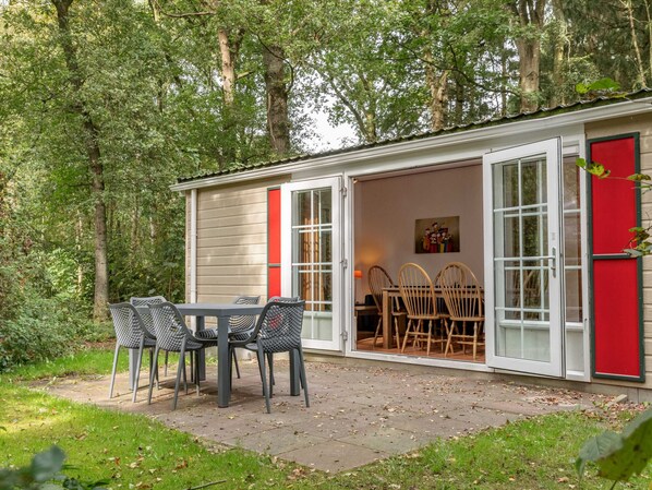 Una pequeña cabaña con un patio, una mesa de comedor con sillas y una puerta roja.