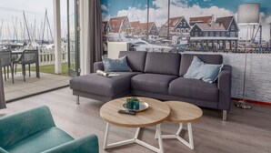 A living room with a grey sofa, two round wooden tables, and teal armchairs. A large mural of a harbor scene is on the wall. - Pet-friendly Garden Getaway (Volendam)