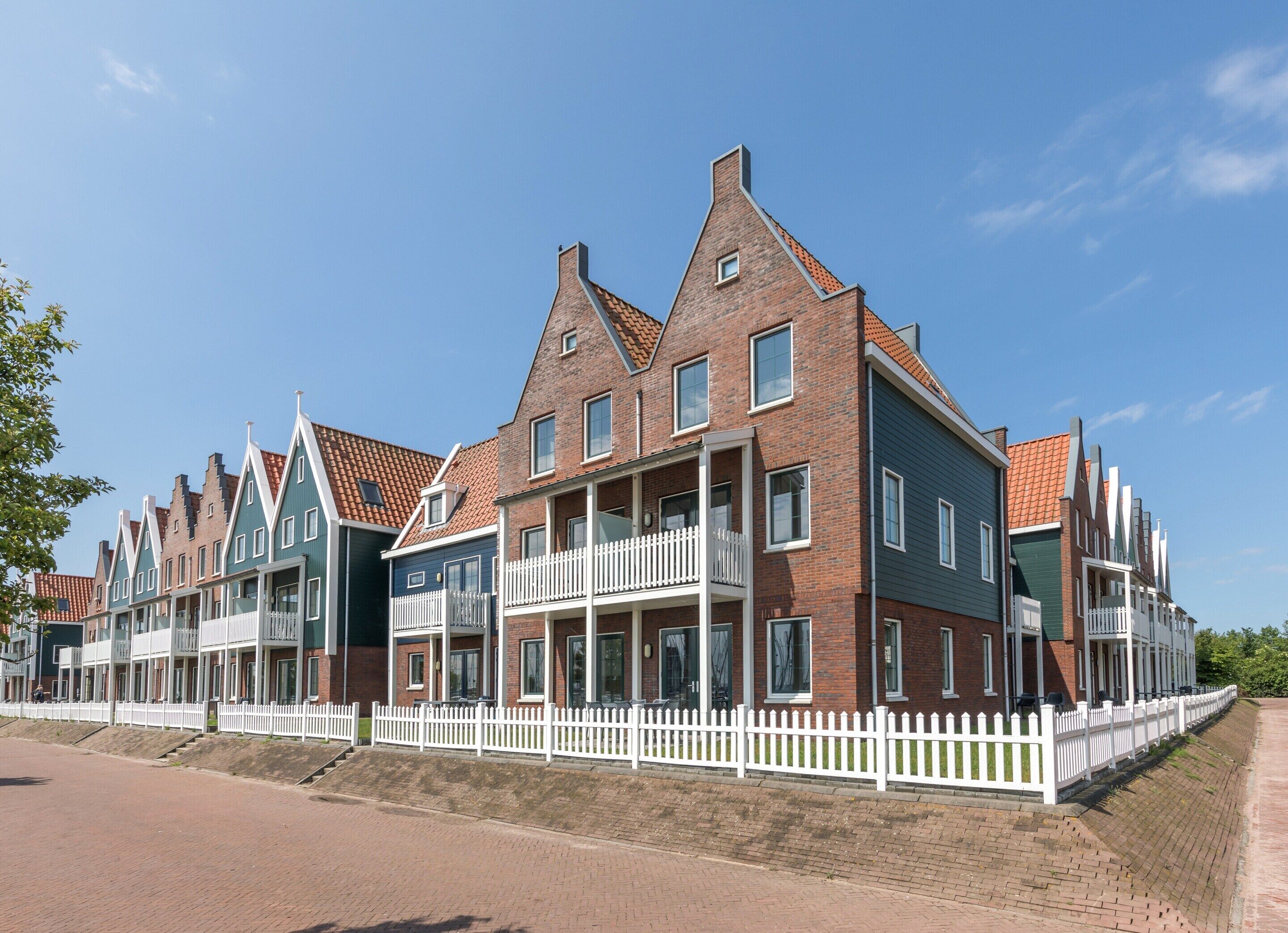 A row of modern brick houses with gabled roofs and white picket fences.