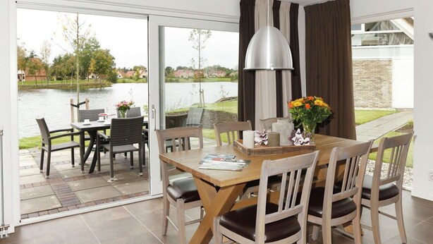 A dining area with a wooden table and chairs, a pendant light, and a view of a lake through a sliding glass door. - Spacious Holiday Home With Garden (Tynaarlo)