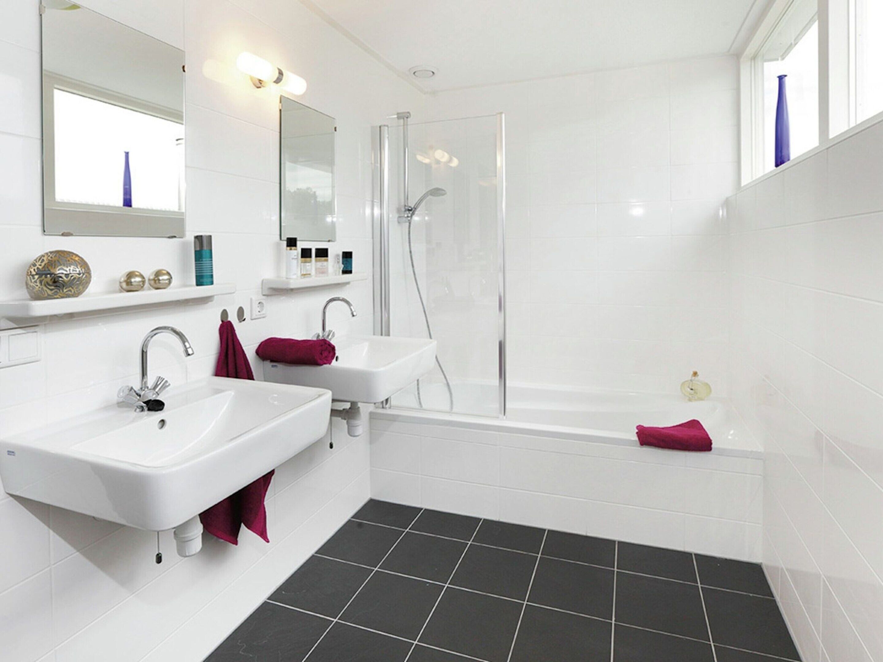 A modern bathroom with two white sinks, a bathtub, and a shower.