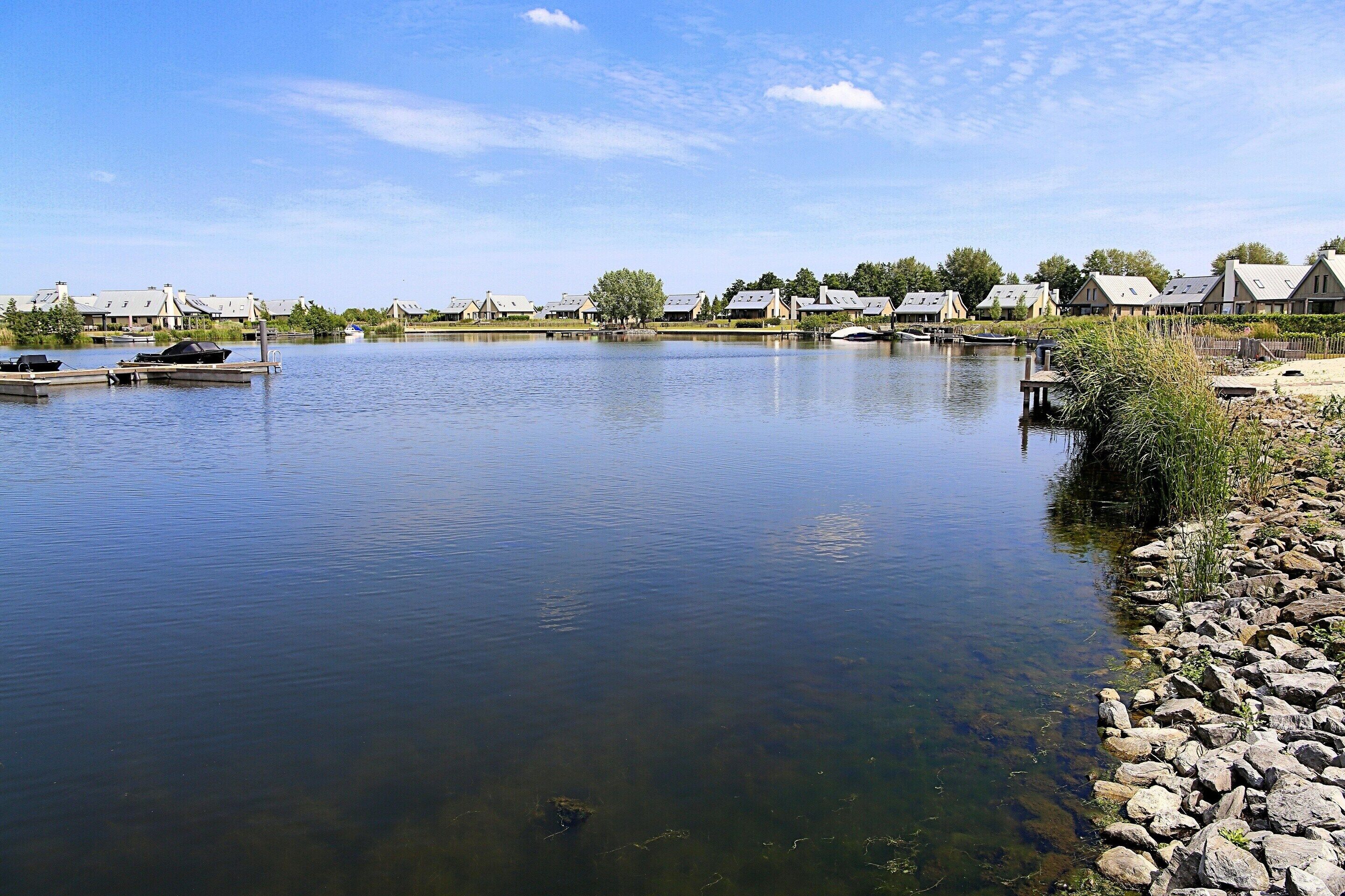 A calm lake with boats docked, surrounded by houses with sloped roofs and a clear sky.
