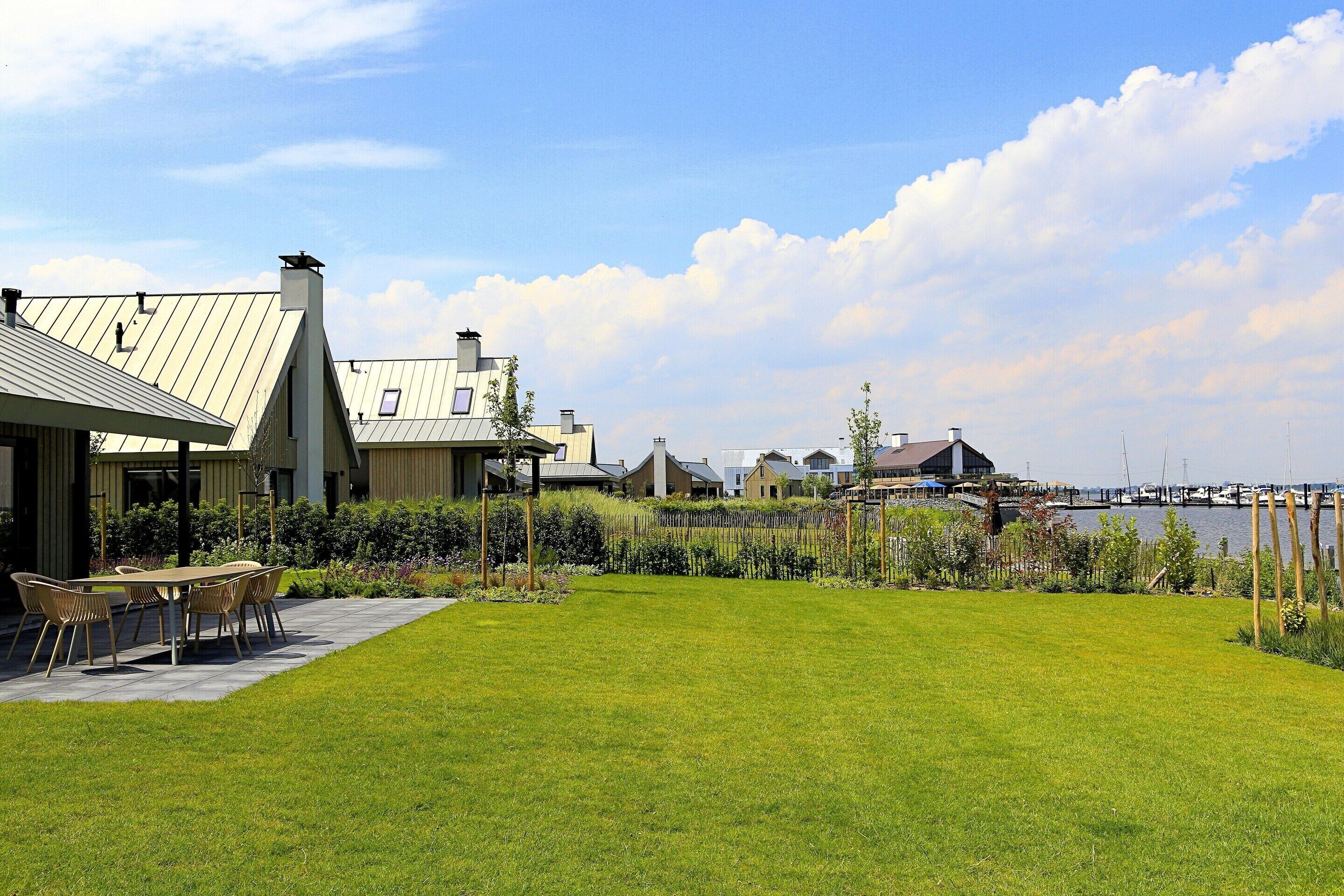 A residential area with a grassy lawn, a dining table with chairs, and a view of a body of water with boats in the distance.