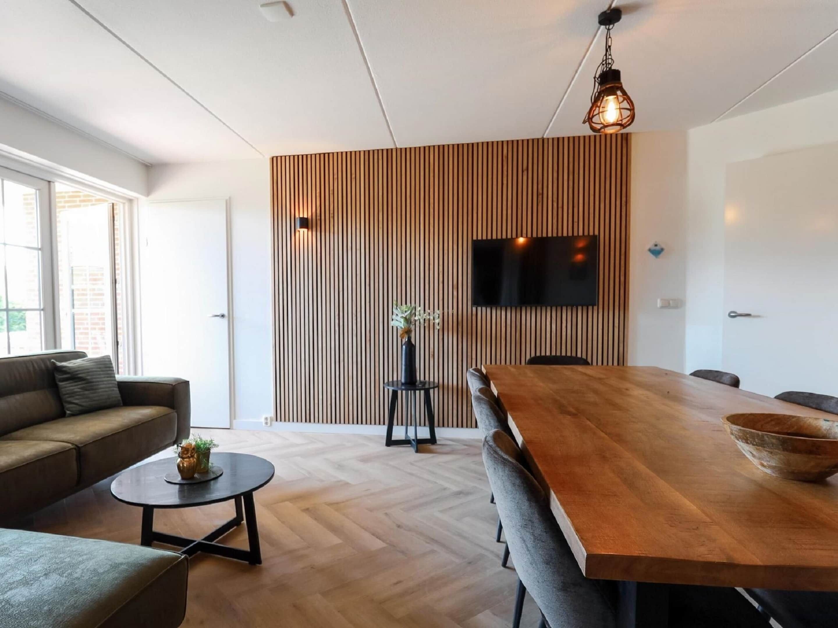 Una sala de estar moderna con un panel de pared de madera, un televisor de pantalla plana, una mesa de comedor con sillas y un sofá.