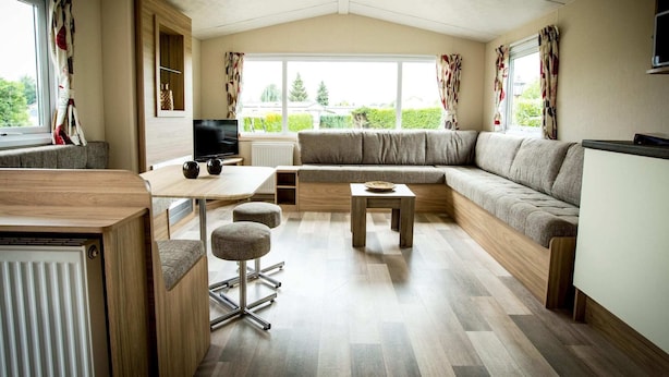 A modern living room with a sectional sofa, a wooden dining table, and a TV. - Apartment in Netherlands Near key Attractions (Udenhout)