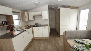 A compact kitchen with white cabinets, a countertop, and a dining area with a table set for two. - Apartment in Netherlands Near key Attractions (Udenhout)