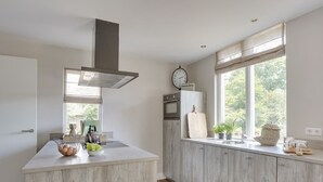 Uma cozinha moderna com ilha central, forno embutido e janela com vista para vegetação.
