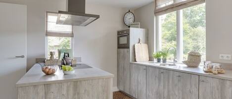 Cocina moderna con una isla central, horno empotrado y ventana con vistas al verdor.