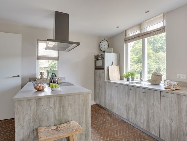 Cocina moderna con una isla central, horno empotrado y ventana con vistas al verdor.