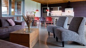 Un salon moderne avec un plafond en bois, un canapé, une table basse et un coin repas avec des chaises, et une cuisine en arrière-plan.