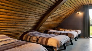 Une chambre confortable dans un chalet en bois, avec trois lits disposés en rangée, un plafond en pente et un mur en briques.