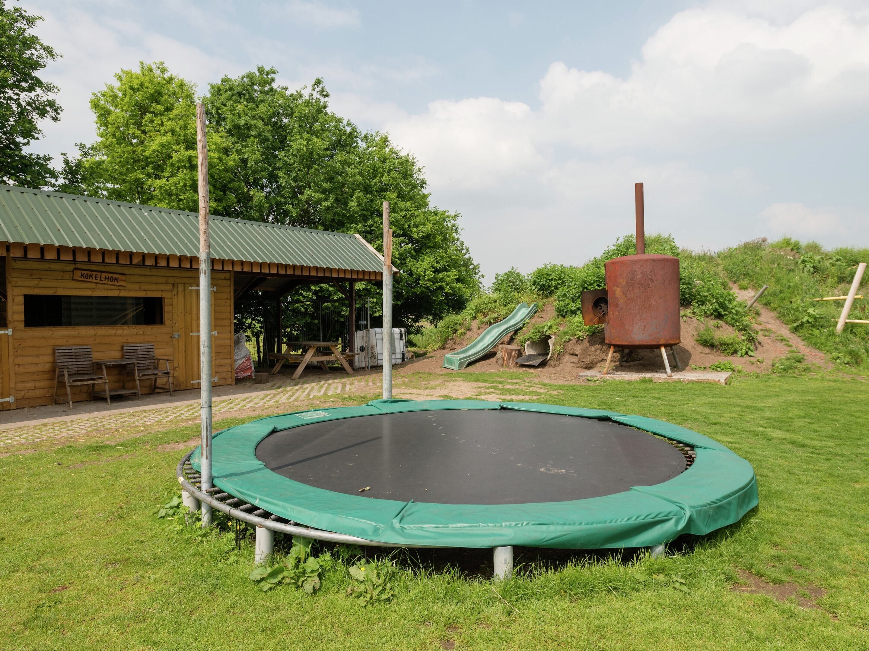 Una cabaña de madera con techo verde, un trampolín, un tobogán y una mesa de picnic.
