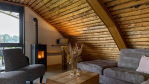 Une pièce confortable de style loft, avec un plafond en pente, une cheminée, un canapé, un fauteuil et une table basse en bois.