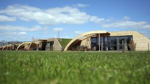 Une rangée de bâtiments modernes, dotés de toits en bois et de grandes fenêtres en verre, se dressant sur un champ verdoyant, avec un ciel dégagé en toile de fond.