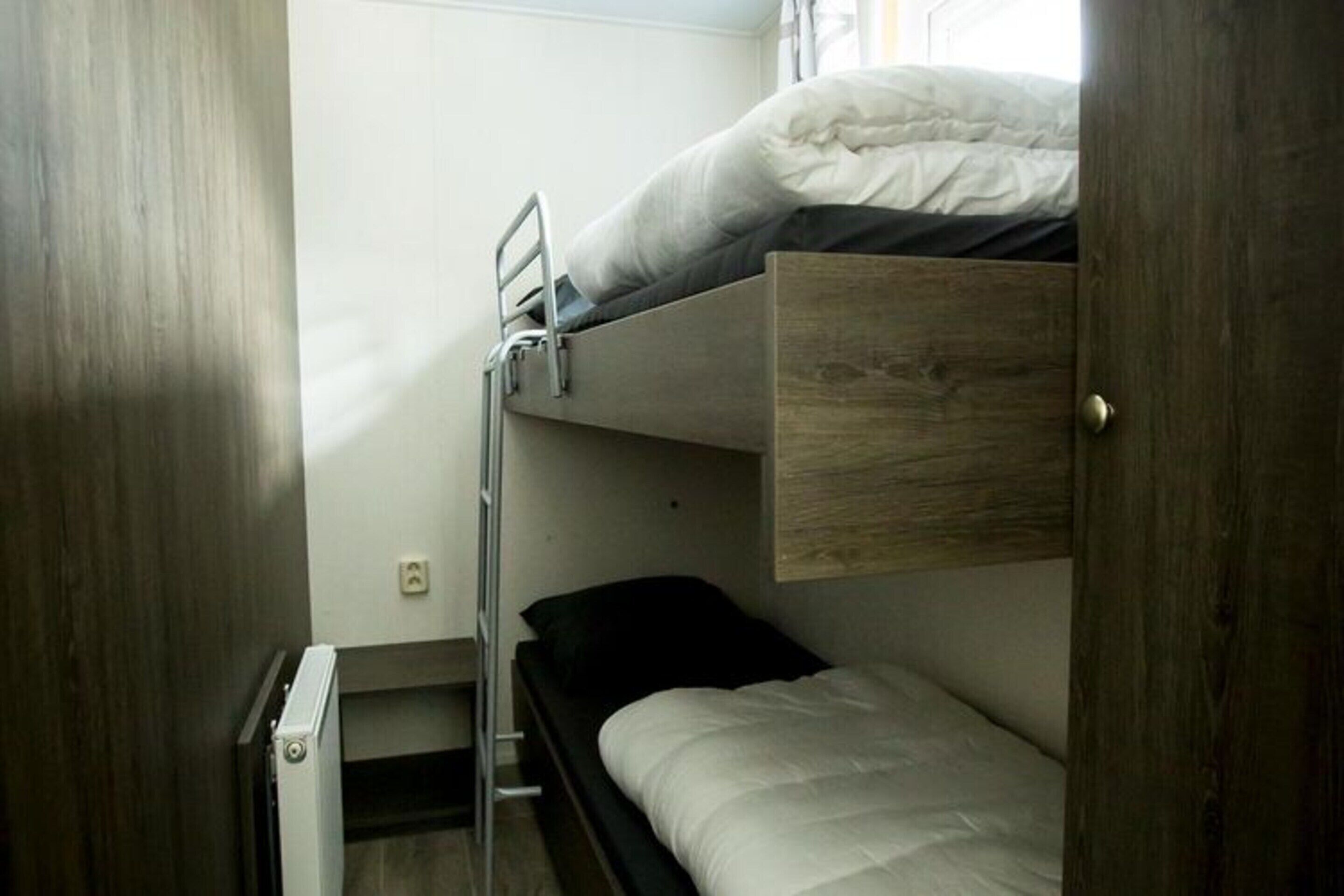 A bunk bed room with a wooden door, a small desk, and a window.