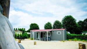 A small, single-story building with a red roof, likely a mobile home or a small cabin, situated on a sandy area with trees in the background. - Chalet Near Loonse and Drunense Duinen (Udenhout)