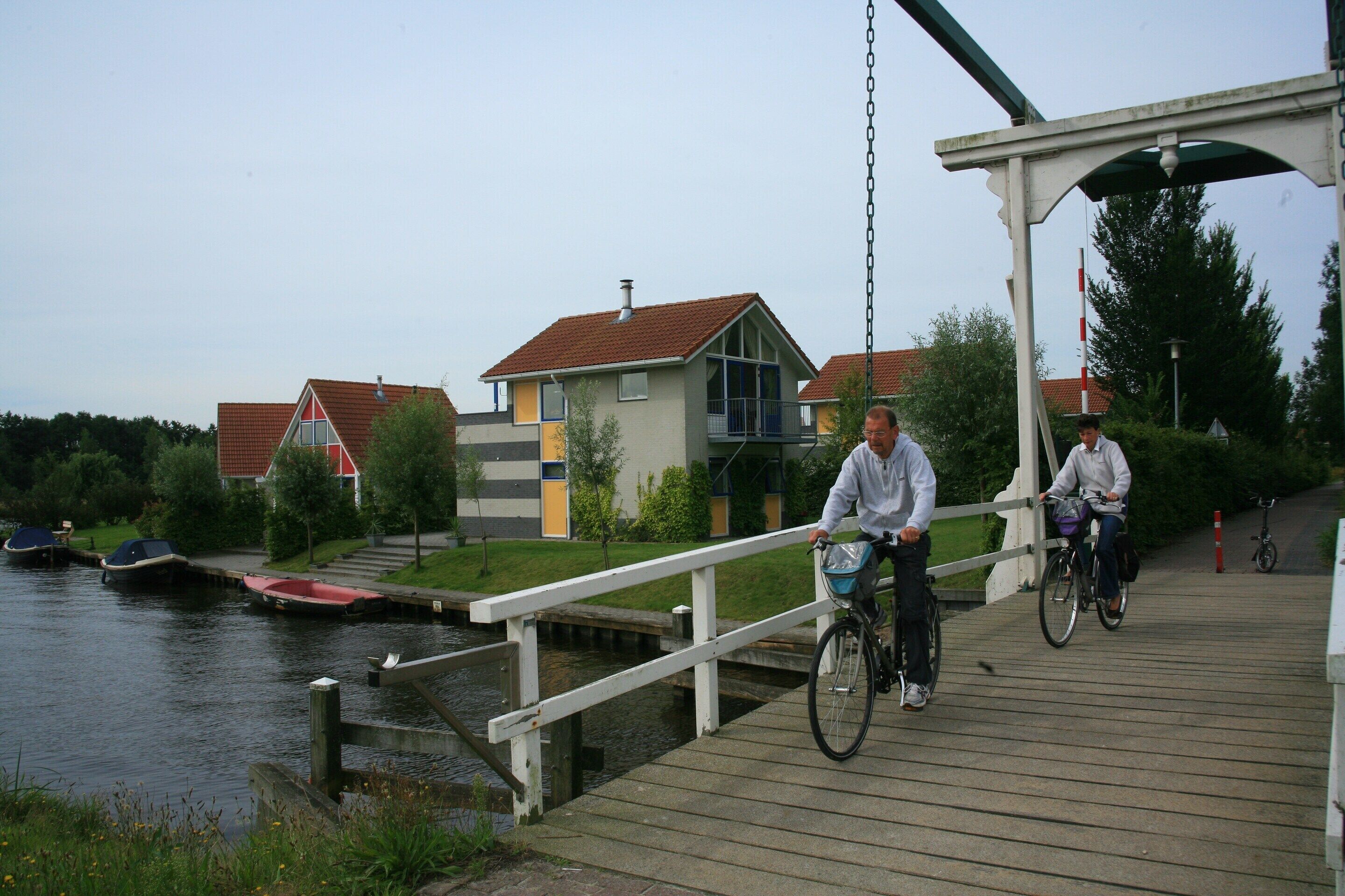 A wooden bridge over water with houses in the background.