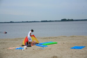 Ein Strand mit einem Zelt, einem Surfbrett und einer Person am Wasser.
