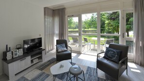 Ein modernes Wohnzimmer mit Fernseher, Sofa, Sesseln und einer Glastür, die auf eine Terrasse im Freien führt.